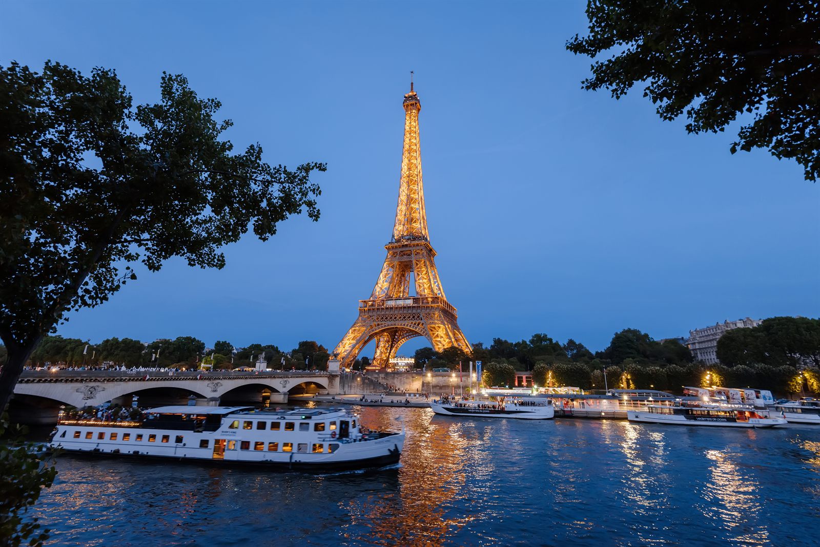 Eiffel Tower lit up at dusk above river boats on the Seine in Paris